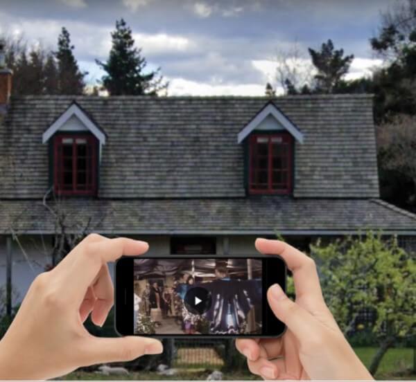 Two hands holding a smartphone in front of a house