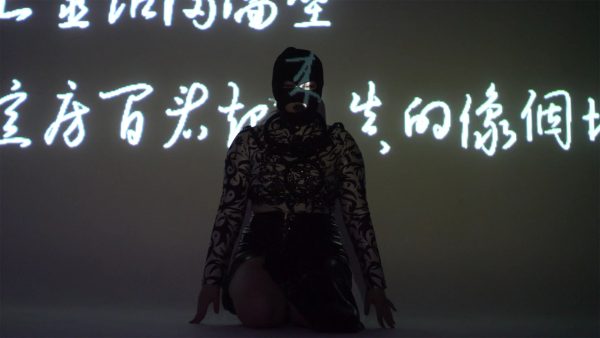 Artist Xi Li performs in a gallery with white chinese characters projected onto the artist in a dark room